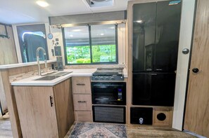 Eine kompakte Küche mit Einbauofen, Mikrowelle und Kühlschrank, ein Fenster mit Blick auf Grünflächen und ein kleines Waschbecken.
