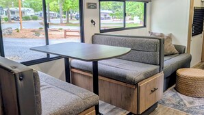 A compact RV interior with a dining area, seating, and a view of the outside. - Cozy riverside camper in peaceful Townsend with AC (Townsend)