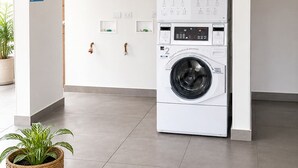 Uma lavanderia moderna com máquina de lavar e secadora empilhadas, um banco e um vaso de planta.