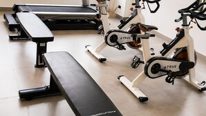 Uma academia com esteira, bicicletas ergométricas e um banco.