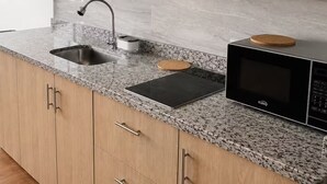 Cozinha com bancada de granito, pia de aço inoxidável, micro-ondas preto e armários de madeira.