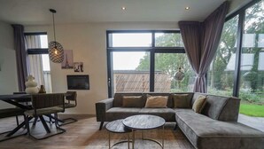 A modern living room with a sectional sofa, a round coffee table, and a dining area with a table and chairs. - Pavilion Maximaal 4 (Kaatsheuvel)