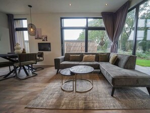 A modern living room with a sectional sofa, a round coffee table, and a dining area with a table and chairs. - Pavilion Maximaal 4 (Kaatsheuvel)