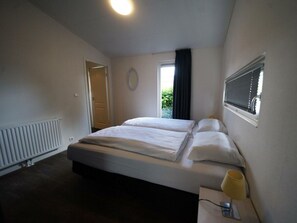 Ein Schlafzimmer mit Bett, Fenster mit Jalousien, Heizkörper und Tür.