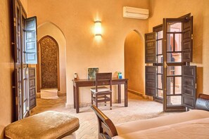 A hotel room with an open door, a desk with a chair, a bench, and a bed. - Luxury Villa Riad & Serene ~ Pool ~ Spa! (Marrakesh)