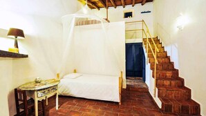 Une chambre à coucher comprenant un lit, une table, une chaise, un escalier et un plafond avec des poutres en bois.