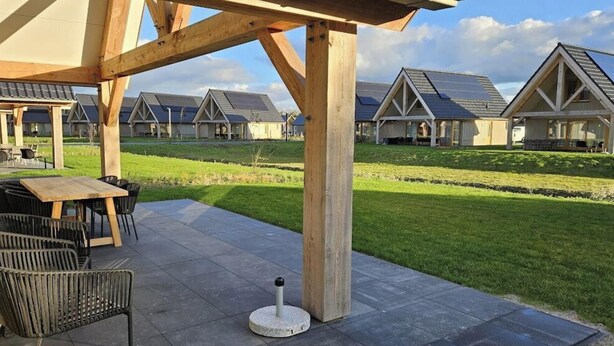 A covered outdoor seating area with a table and chairs, a stone bollard, and a view of multiple houses with pitched roofs. - Villa in Cadzand With Terrace and Wi-fi (Cadzand-Bad)