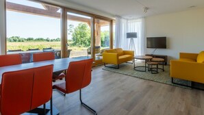 A modern living room with a dining area, large windows, and a flat-screen TV. - Villa in Cadzand With Terrace and Wi-fi (Cadzand-Bad)