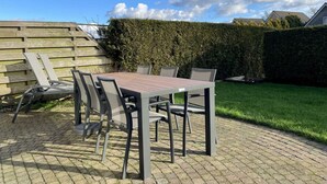 Eine Terrasse im Freien mit Tisch und Stühlen, einem Holzzaun und einer Hecke.