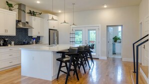 A modern kitchen with white cabinets, a central island with bar stools, pendant lighting, and a view to the outdoors. - Dallas Luxury Smart Home Near Golf, Trails, Tennis, Shopping & Downtown Access (Dallas)
