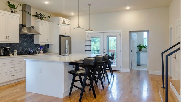 A modern kitchen with white cabinets, a central island with bar stools, pendant lighting, and a view to the outdoors. - Dallas Luxury Smart Home Near Golf, Trails, Tennis, Shopping & Downtown Access (Dallas)