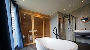 Un baño moderno con una bañera independiente, un box de ducha con mampara de vidrio y una puerta corredera de madera que da acceso a la zona de ducha.