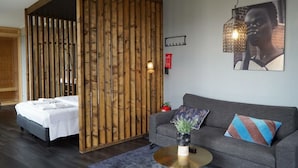 Una habitación con una cama, un sofá, una mesa redonda con una planta y una lámpara de pared.