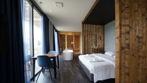 Una habitación de hotel moderna con una cama, un escritorio con silla, una bañera y ventanas amplias.