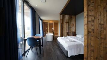 Una habitación de hotel moderna con una cama, un escritorio con silla, una bañera y ventanas amplias.