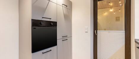 A compact kitchen with a built-in oven and a sliding door leading to a balcony with string lights.