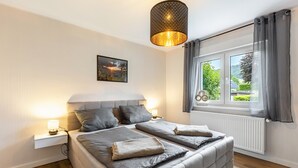 Ett sovrum med en säng, sängbord, ett fönster med gardiner, ett element och en hängande lampa.