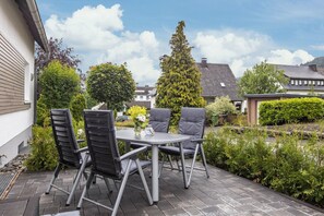 Eine Terrasse im Freien mit einem runden Tisch und vier Stühlen, umgeben von viel Grün und Blick auf Wohnhäuser.