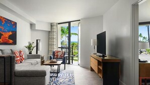 A modern living room with a sofa, coffee table, and TV. There's a balcony with a view of palm trees and the ocean. - Marriott Waikoloa Ocean Club resort in Waikoloa Village with AC and OCEAN VIEW (Waikoloa Village)