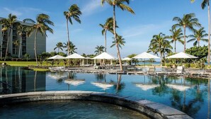 A pool area with lounge chairs and umbrellas, surrounded by palm trees and a hotel building. - Marriott Waikoloa Ocean Club resort in Waikoloa Village with AC and OCEAN VIEW (Waikoloa Village)