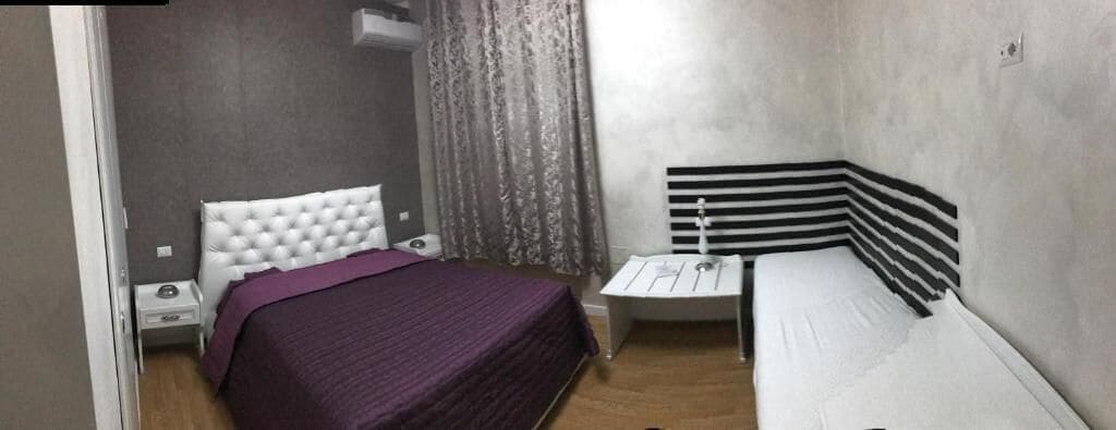 A bedroom with two beds, a nightstand, a small table, and a window with curtains.