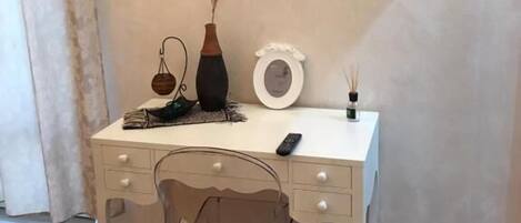 A white desk with a television mounted on the wall, a vase, and a small table with a candle.