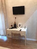 Un escritorio blanco con un televisor montado en la pared, un florero y una mesita con una vela.