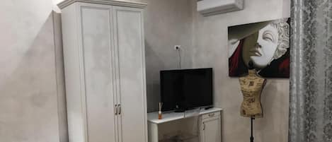 A bedroom with a wardrobe, a desk with a TV, a mannequin, and a bed.