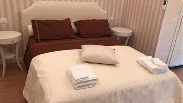 Un lit bien fait, avec une couette blanche, deux oreillers marron et des serviettes blanches pliées.