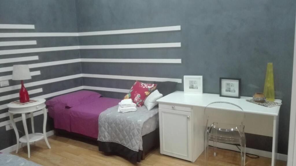 Un dormitorio con cama, mesita de noche, lámpara y escritorio con silla.