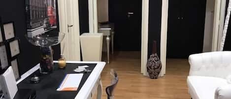 Una habitación con escritorio, silla, sofá blanco y puerta que da a otra estancia.