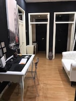 Una habitación con escritorio, silla, sofá blanco y puerta que da a otra estancia.
