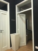 Una habitación con una puerta blanca, un bote de basura blanco y una pared negra con un cartel.