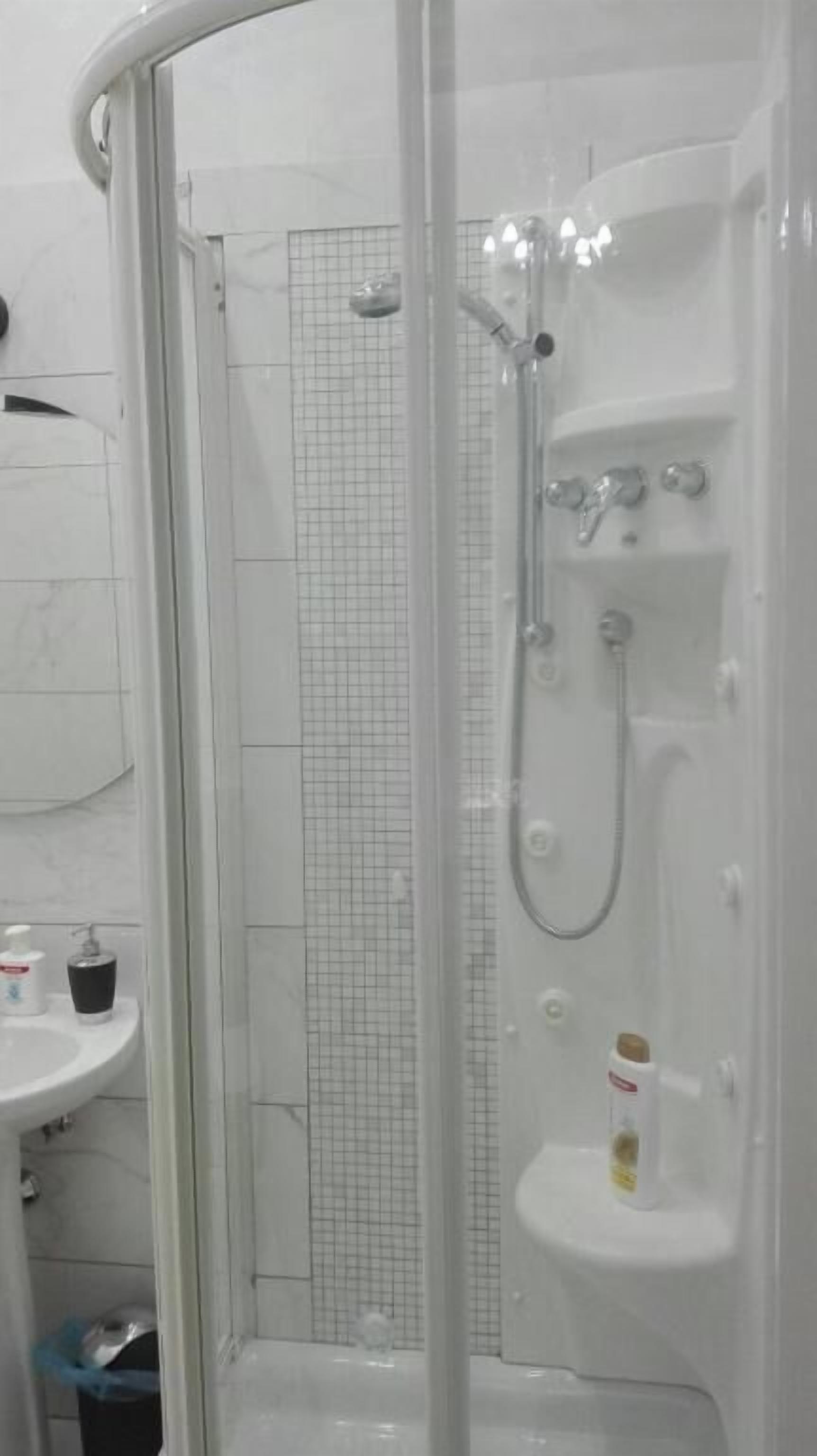 Un box de ducha con puerta de vidrio, pared con azulejos blancos y un lavabo con una taza encima.