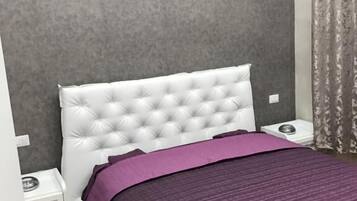 Un dormitorio con cabecera capitonada, colcha morada, mesita de noche y aire acondicionado instalado en la pared.