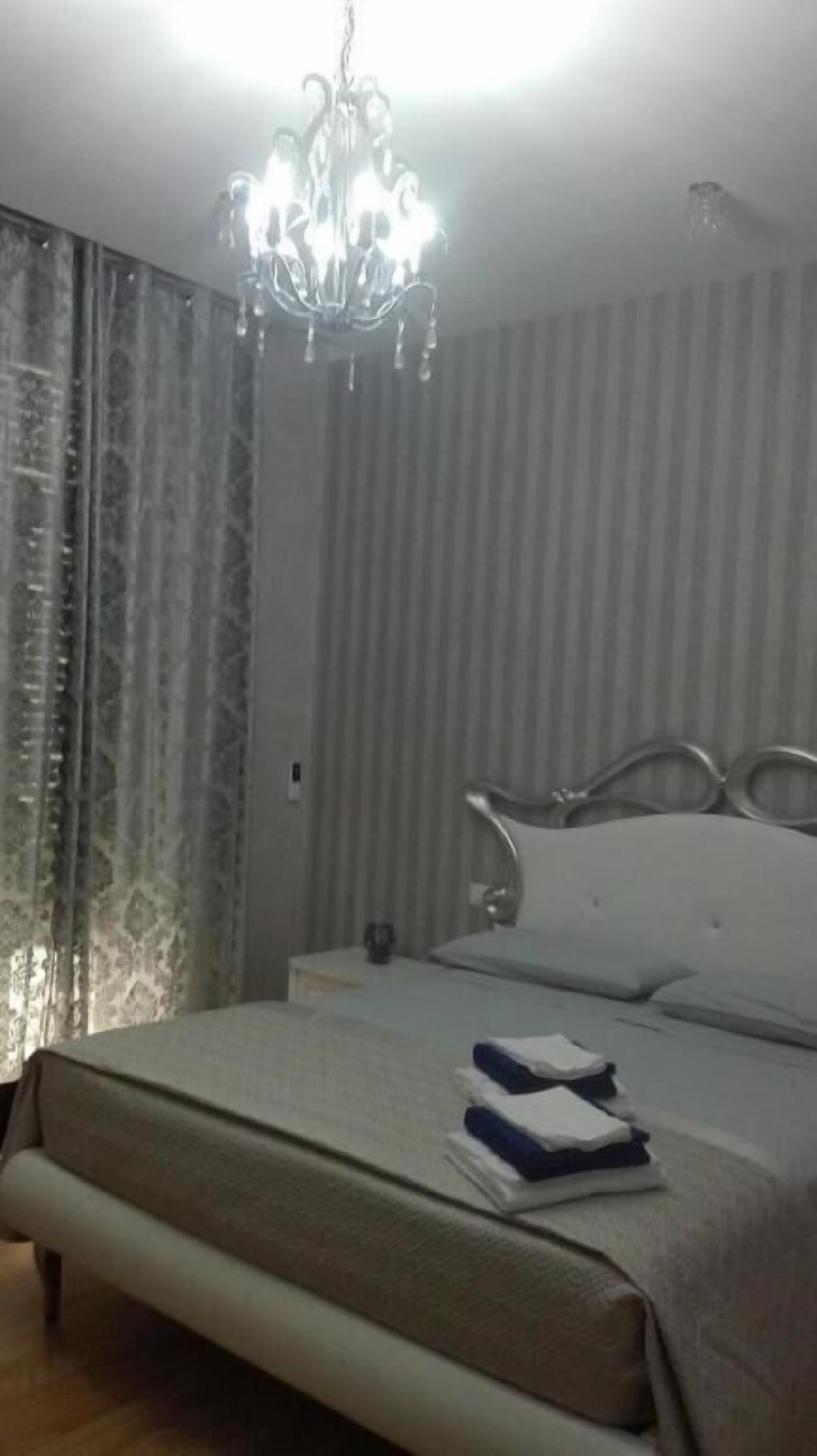 A hotel room with a bed, a nightstand, a lamp, and a chandelier.