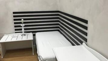 A single-bed room with a striped headboard, a bedside table, and a chair.