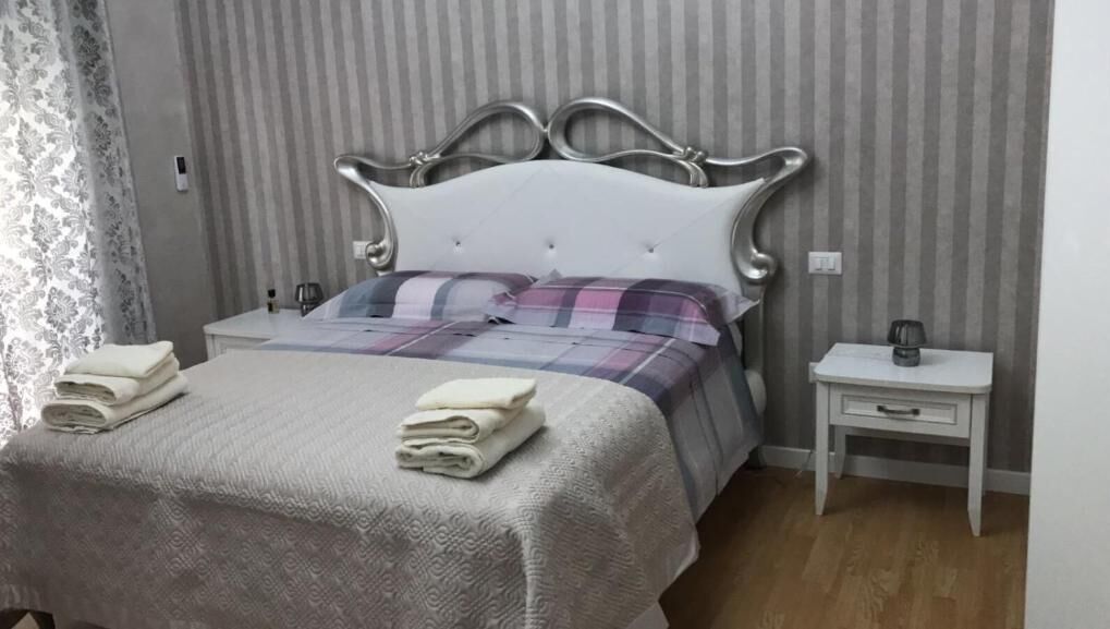 A neatly made bed with a white headboard, a bedside table with a lamp, and a folded towel on the bed.