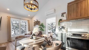A modern kitchen with an oven, a dining area with a round table and chairs, and a large window with a view of trees.