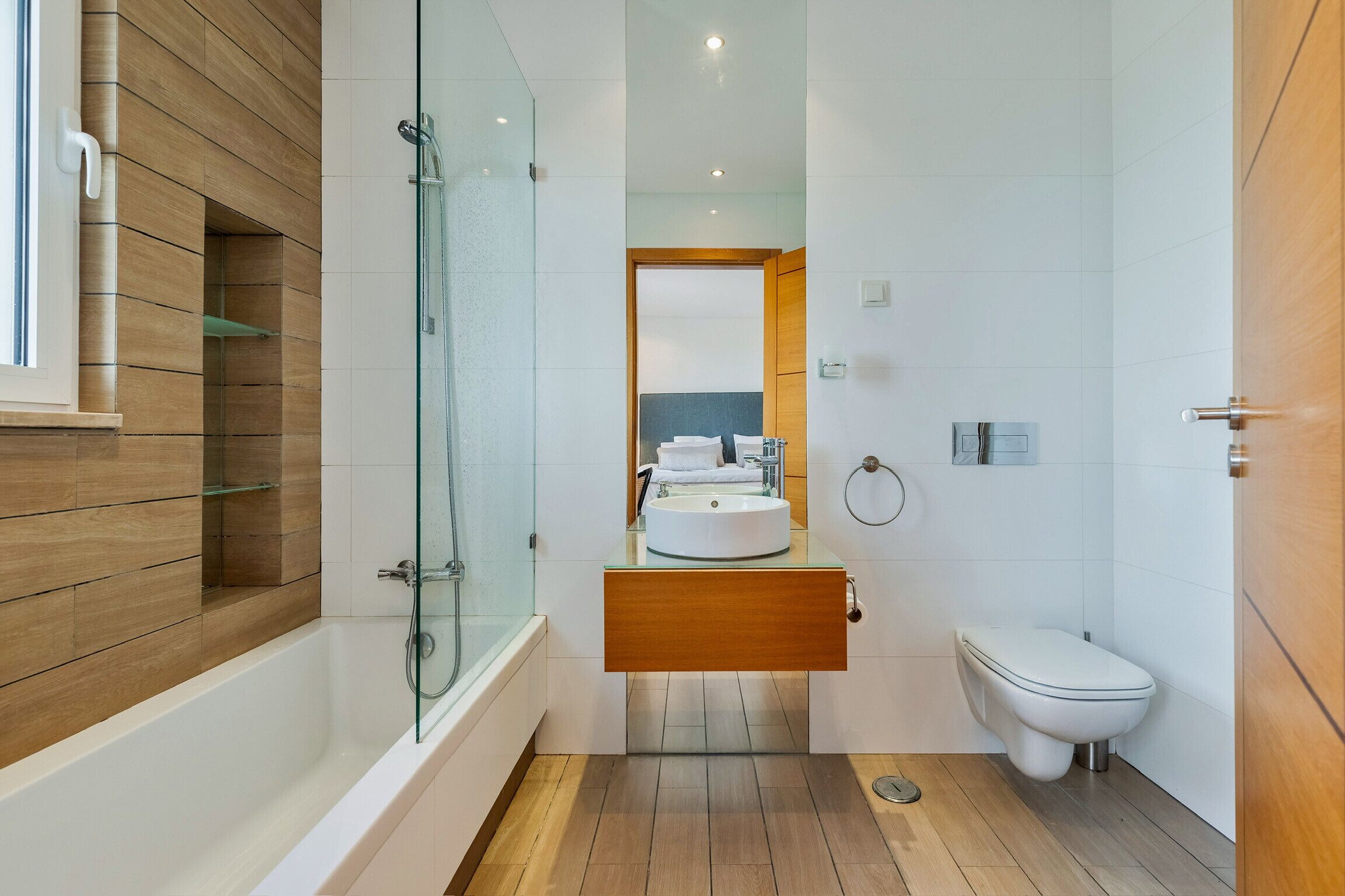 Un baño moderno con ducha de vidrio, tocador de madera, inodoro blanco y un espejo grande.
