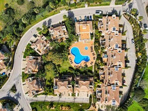 Eine Luftaufnahme eines Wohngebiets mit einem zentral gelegenen Schwimmbad, umgeben von Häusern mit einheitlicher Architektur.