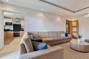 Ein modernes Wohnzimmer mit einer Eckcouch, einem runden Couchtisch und einer Küche im Hintergrund.