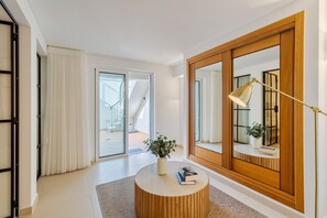 Ein modernes Wohnzimmer mit einem runden Holztisch, einer Topfpflanze, einem Buch, einer Stehlampe und einem großen Spiegel.