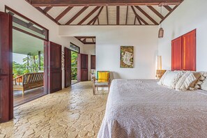 Ein Schlafzimmer mit einem großen Bett, Holzbalkendecke, einem Gemälde an der Wand und Blick durch eine offene Tür.