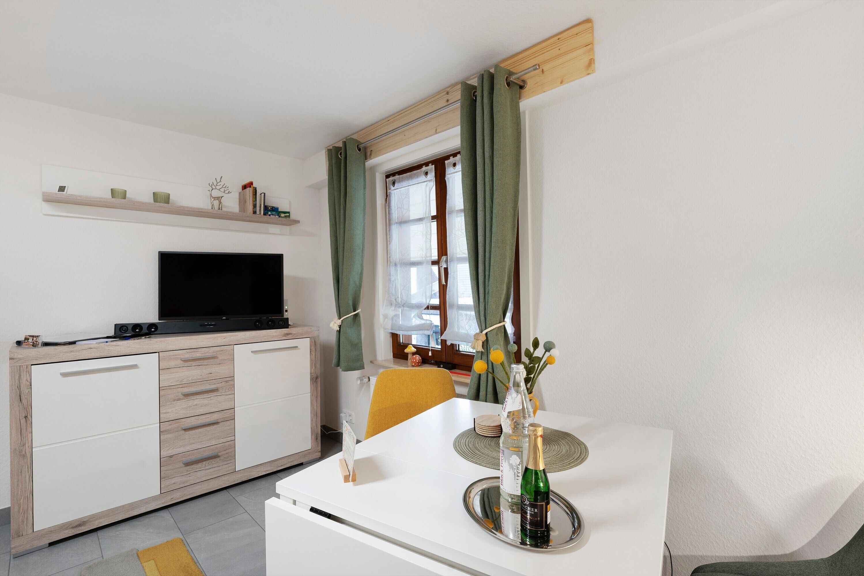 Ein modernes Wohnzimmer mit Flachbildfernseher, Esstisch in Weiß und einer Couch.
