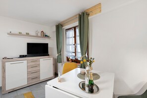 Ein modernes Wohnzimmer mit Flachbildfernseher, Esstisch in Weiß und einer Couch.