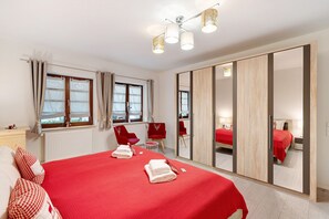 Une chambre d’hôtel avec un grand lit, une armoire avec un miroir, un coin salon avec des fauteuils et une fenêtre avec des rideaux.