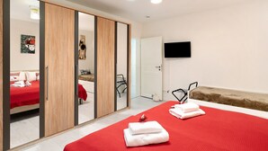 A hotel room with a bed, a red blanket, a wooden wardrobe, a mirror, a television, and a small sofa. - Apartment 'Ferienwohnung Höflelounge' with Mountain View, Balcony and Wi-Fi (Oppenau)