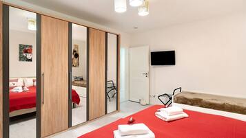 Una habitación de hotel con una cama, un edredón rojo, un armario de madera, un espejo, un televisor y un pequeño sofá.
