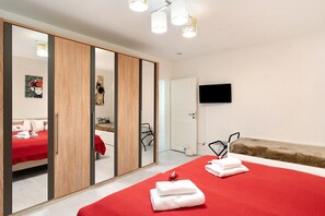 Ein Hotelzimmer mit einem Bett, einer roten Decke, einem Holzschrank, einem Spiegel, einem Fernseher und einem kleinen Sofa.